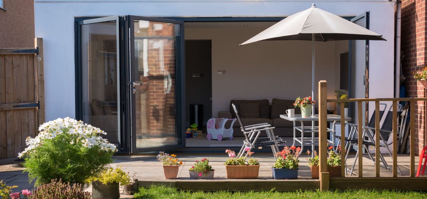 External view of Origin bifold doors with garden table and umbrella outside on sunny day